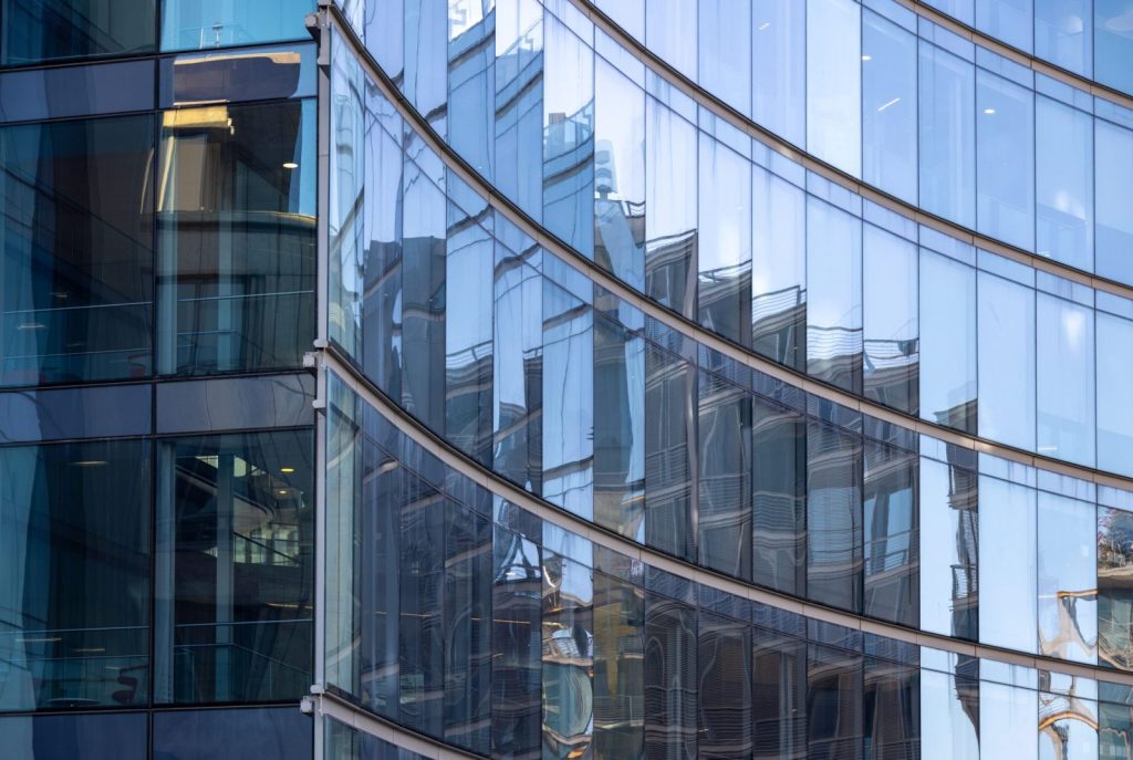 Close-up shot of a modern curved glass facade reflecting surrounding buildings in an urban setting.